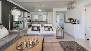 Un salon moderne avec un canapé, des fauteuils, une table basse et une cuisine en arrière-plan.