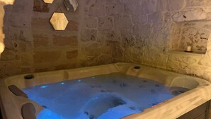 A stone-walled room with a bathtub filled with water and blue lighting.