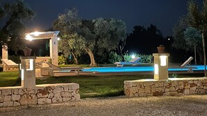 A nighttime pool area with lounge chairs and a stone structure.