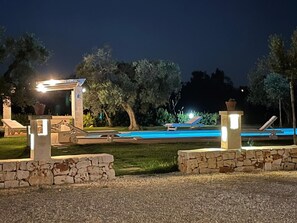 A nighttime pool area with lounge chairs and a stone structure.