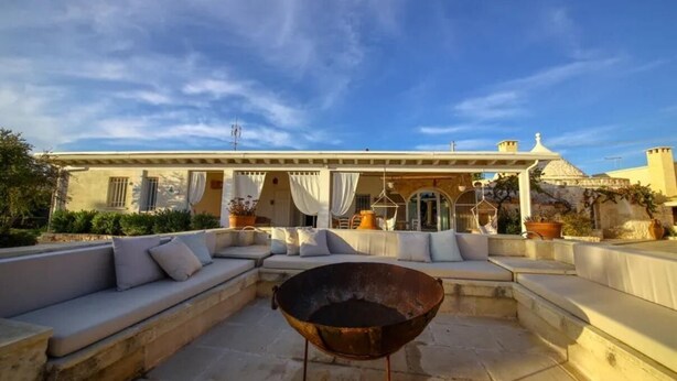 An outdoor seating area with a large metal bowl, cushioned benches, and a covered patio.