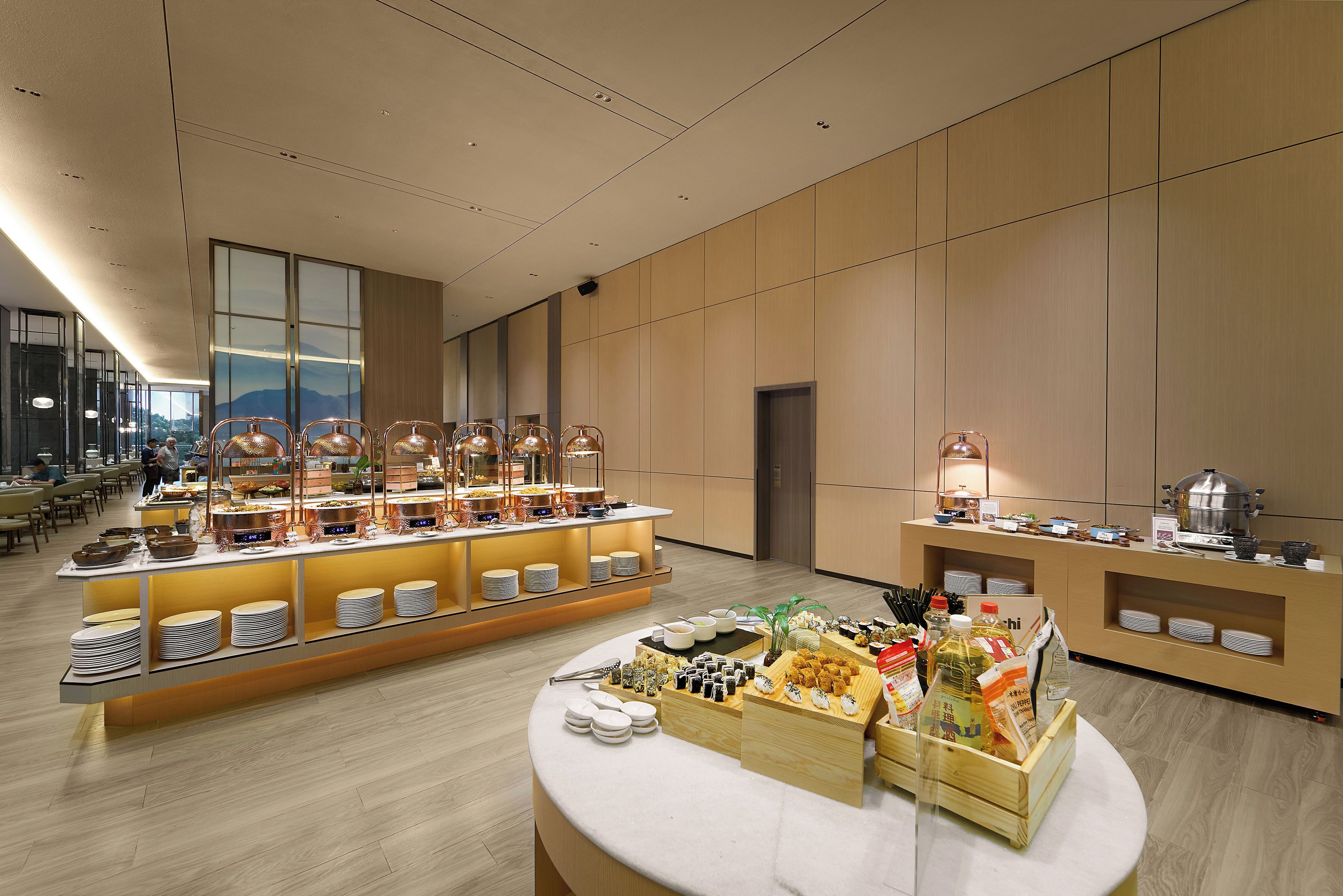 Ein reichhaltiges Buffet mit verschiedenen Speisen und Getränken, ein Sitzbereich mit Tischen und Stühlen sowie ein großes Fenster mit Blick ins Freie.