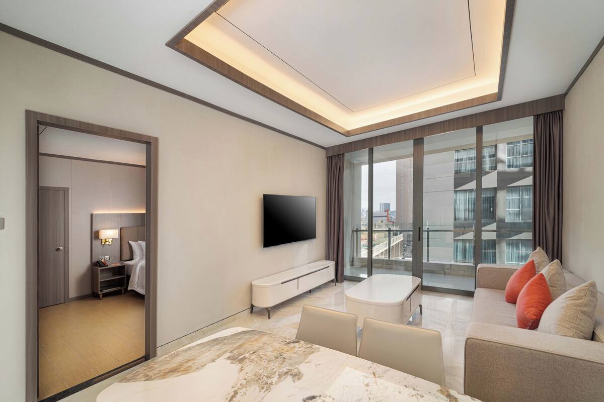 Een moderne hotelkamer met een groot raam, een flatscreen televisie, een bank, een eettafel en een inloopkast.