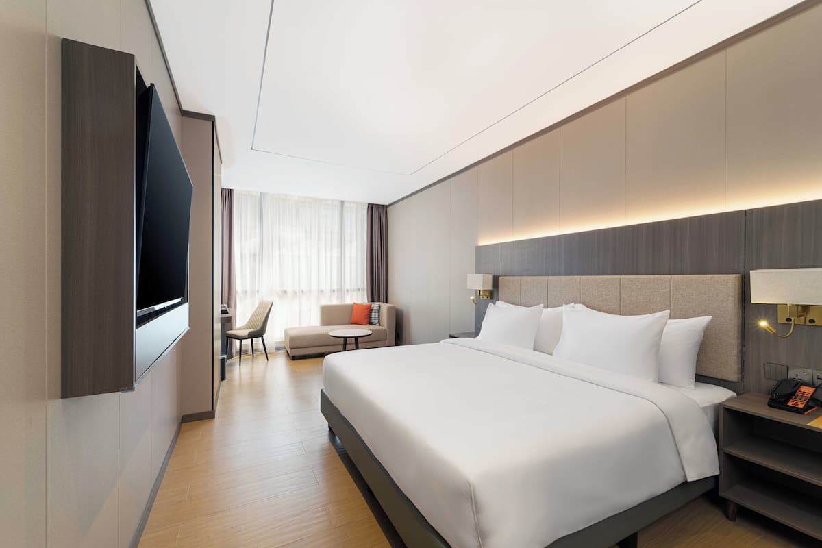 Een moderne hotelkamer met een groot bed, een flatscreen televisie aan de muur, een bureau met stoel en een nachtkastje met lamp.