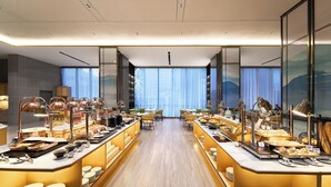 A modern hotel breakfast area with a long counter, multiple seating options, and a view of the city through large windows. - Harris Hotel & Suites Nagoya Batam (Batam)