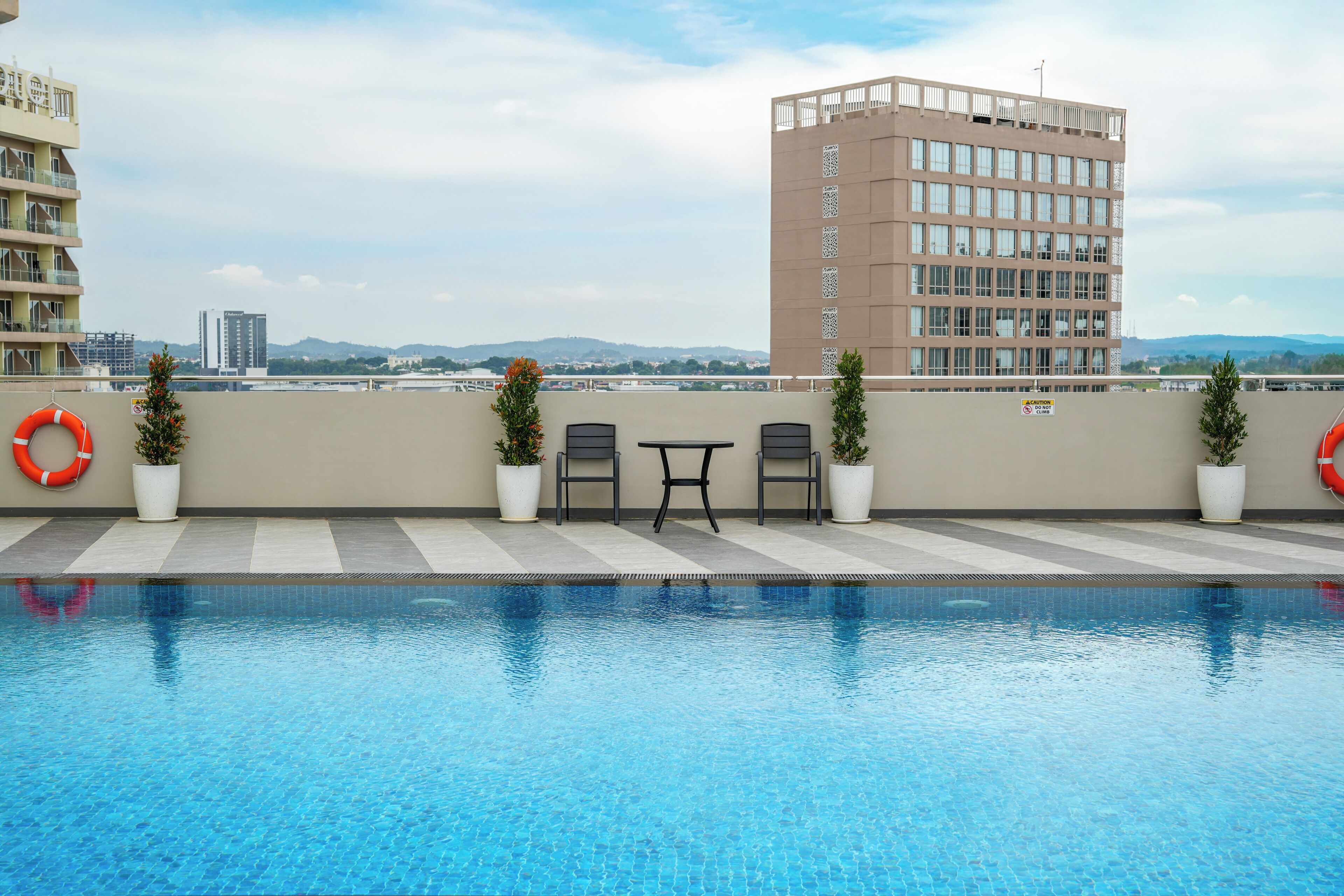 A rooftop pool area with a clear view of the cityscape, including a tall building and distant hills.