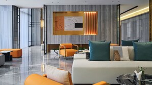 A modern hotel lobby with a white sofa, orange armchairs, and a large wall art piece. - Harris Hotel & Suites Nagoya Batam (Batam)