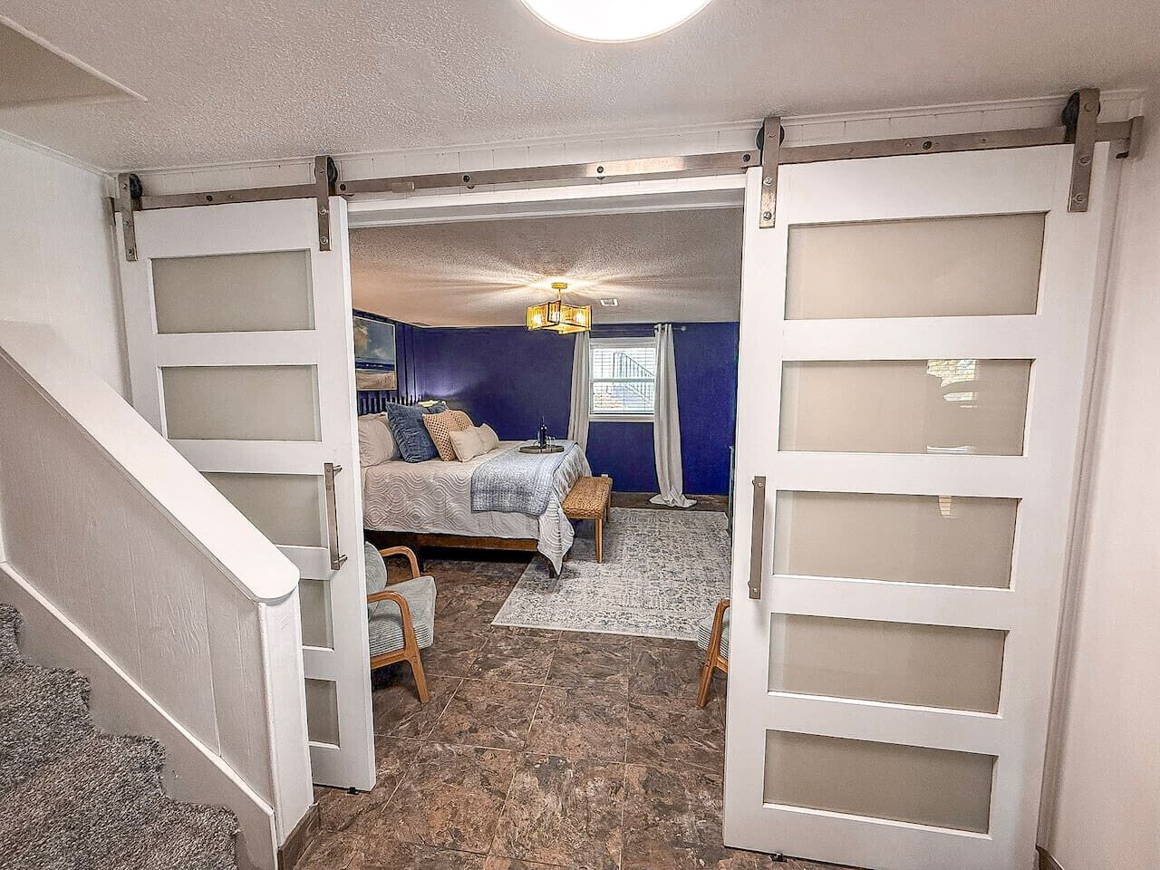 A bedroom with a bed, a chair, a small table, and a window.