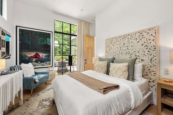 A modern bedroom with a large bed, a blue sofa, and a large window with a view of greenery.
