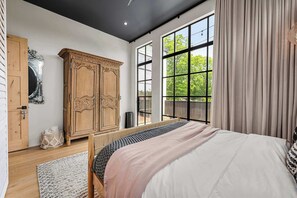 A bedroom with a large bed, wooden wardrobe, and a view through floor-to-ceiling windows.