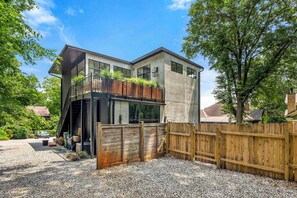 A modern two-story house with a balcony, a wooden fence, and a gravel driveway.