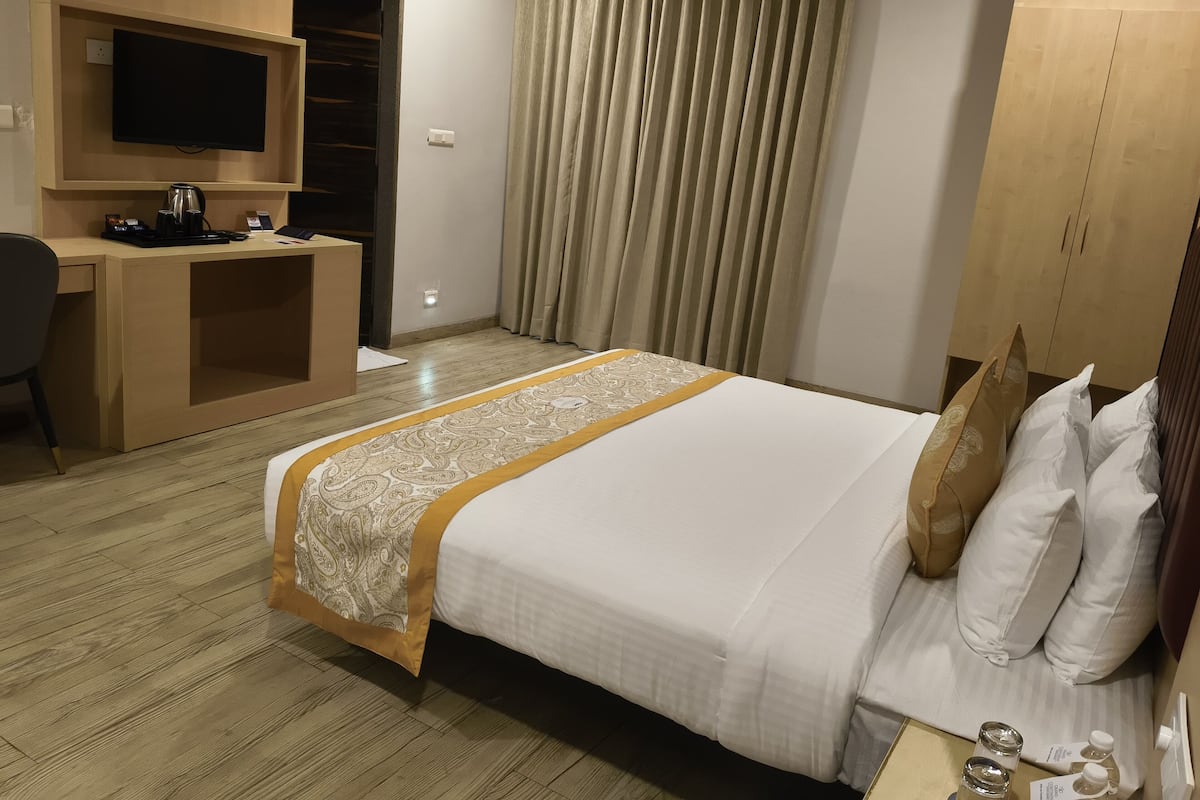 Ein Hotelzimmer mit einem Bett, einem Schreibtisch mit Fernseher, einem Kleiderschrank und einem Fenster mit Vorhängen.
