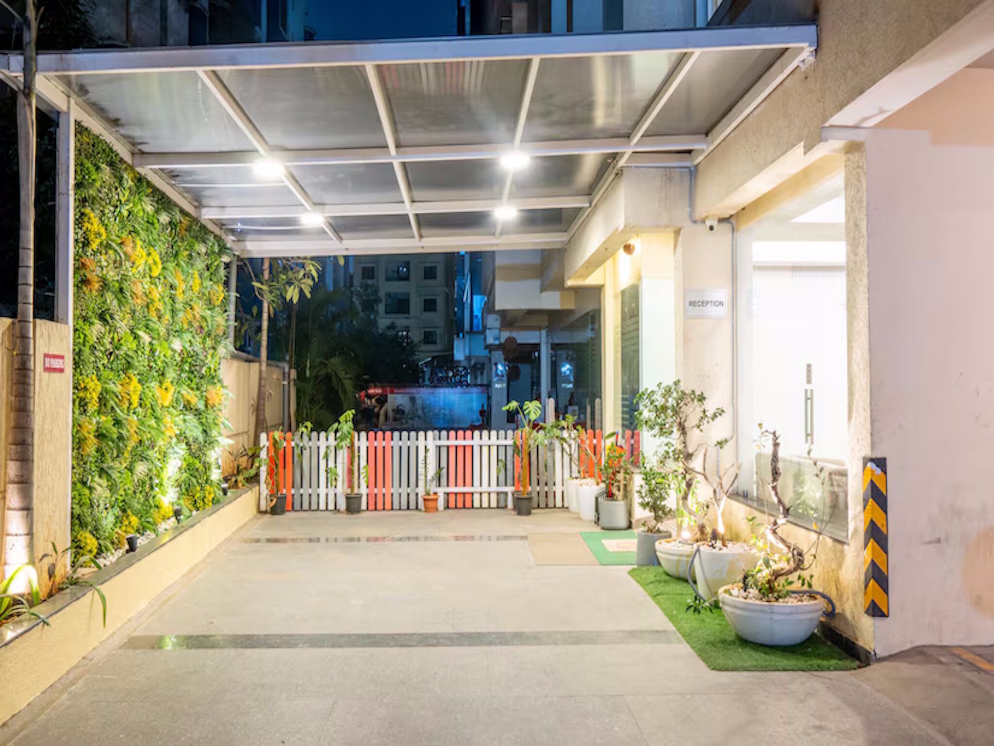 A hotel entrance with a reception desk, a green vertical garden, and potted plants.