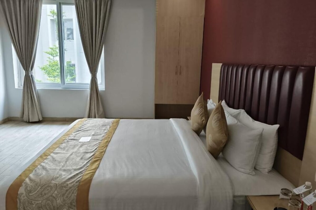 A hotel room with a bed, curtains, a headboard, and a window.