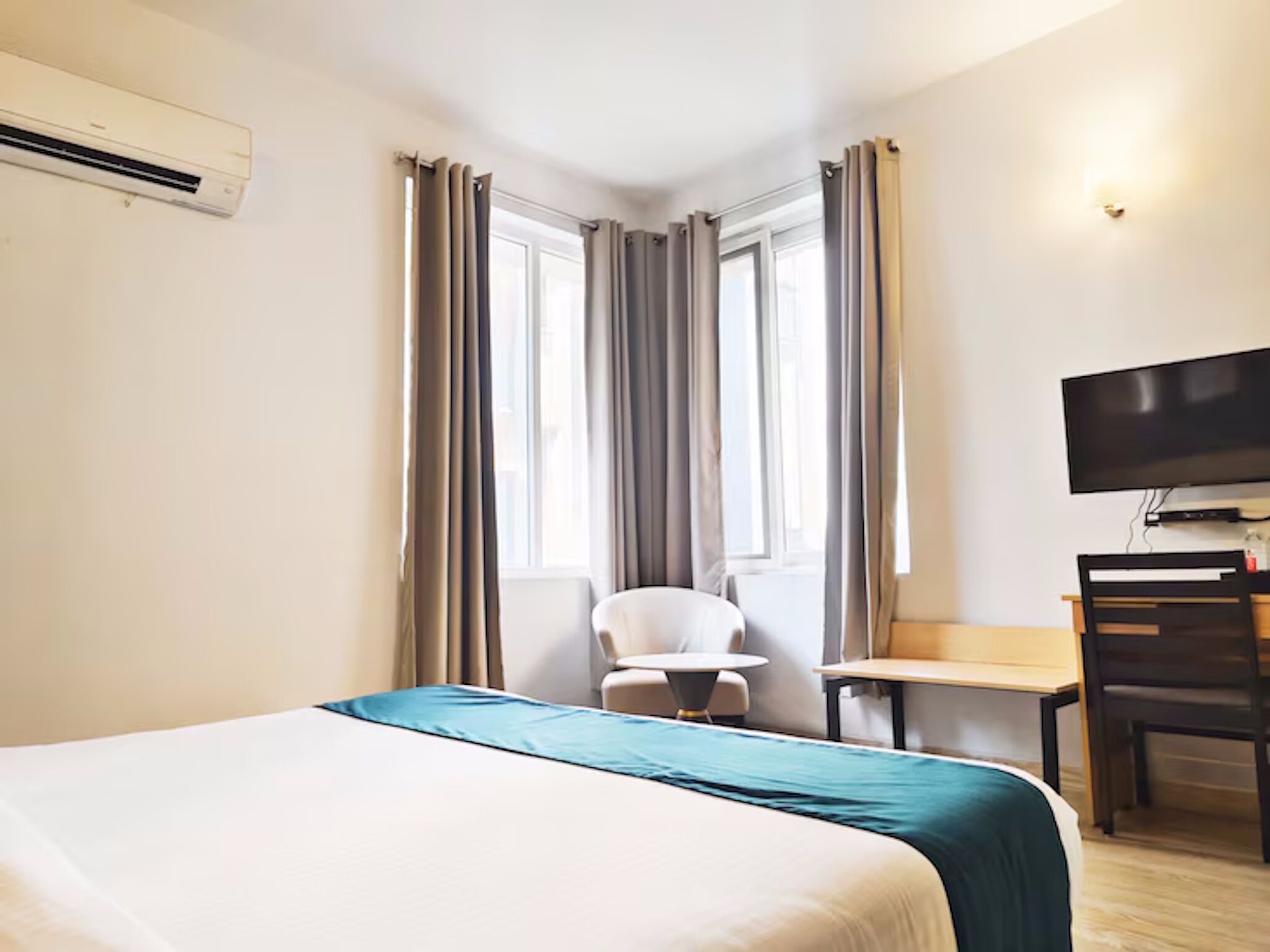 Una camera d'albergo con un letto, una scrivania, una sedia, una televisione e una finestra con tende.