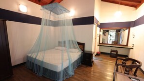 A bedroom with a bed under a mosquito net, a wooden floor, a small table with a chair, and a mirror on the wall. - Kumudu Valley Resort (Nainamadama)