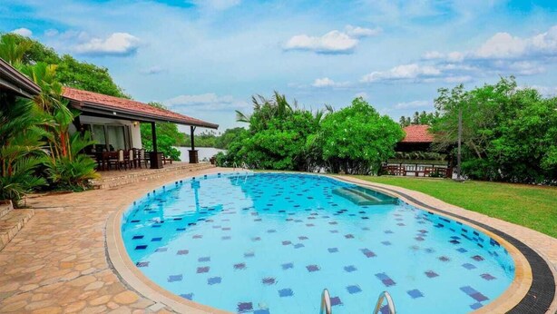 A swimming pool with a stone deck, surrounded by greenery and a covered seating area. - Kumudu Valley Resort (Nainamadama)