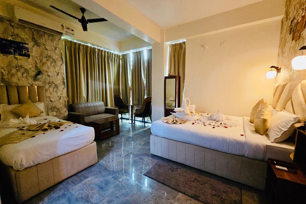 Une chambre d’hôtel avec deux lits, un canapé, une petite table et un ventilateur de plafond.