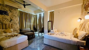A hotel room with two beds, a sofa, a small table, and a ceiling fan.