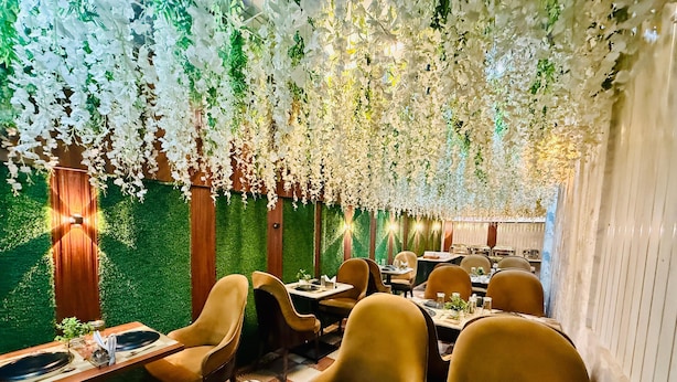 A restaurant with tables set for dining, surrounded by hanging floral decorations and green foliage.