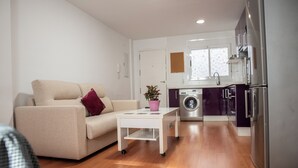 En kompakt opholdsstue med sofa, lille sofabord, vaskemaskine og køleskab.