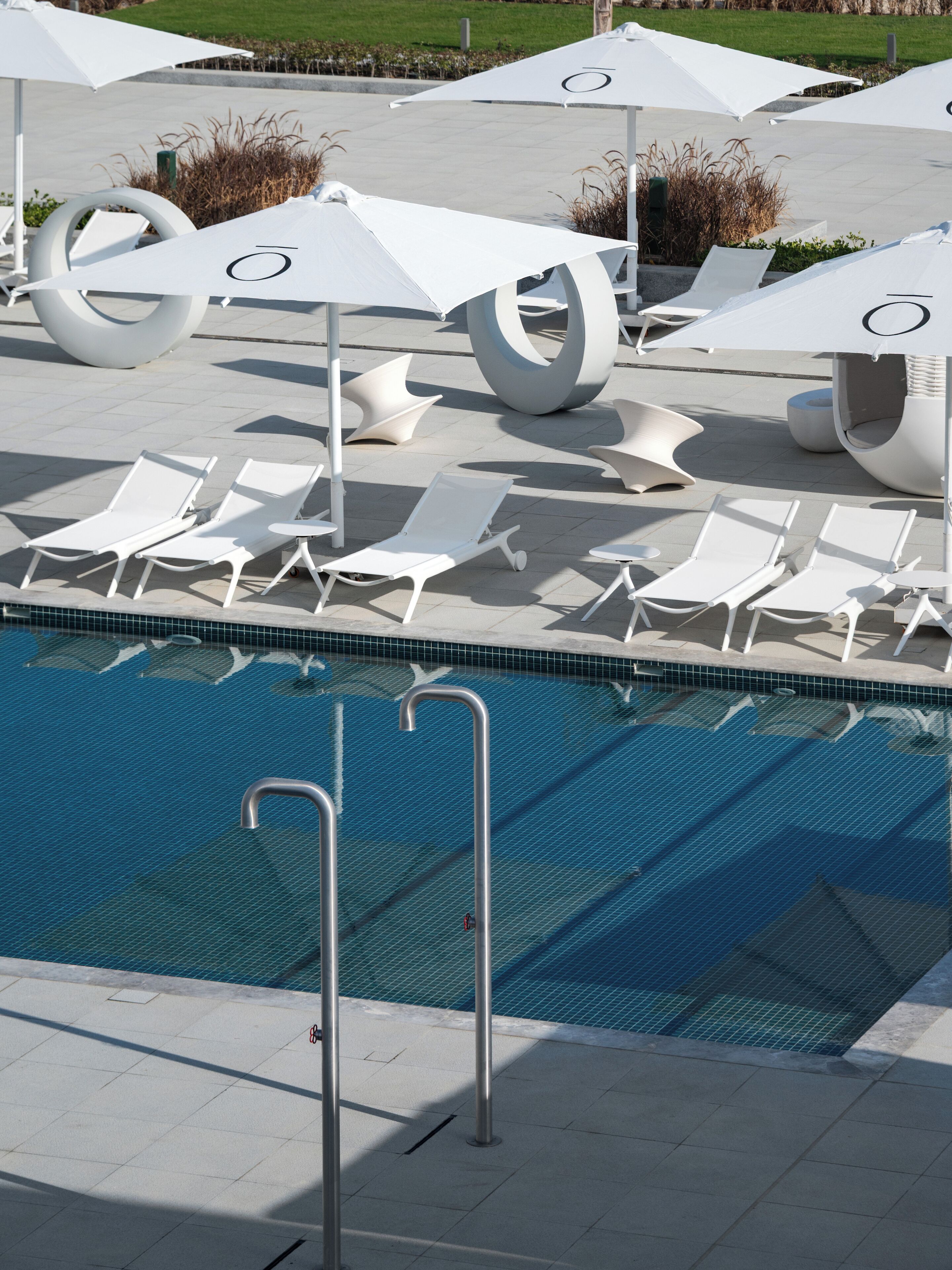 A pool area with white lounge chairs and umbrellas, a clear blue pool, and a tiled deck.