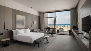 A modern hotel room with a large bed, a seating area, a TV, and a balcony with a view of the beach. - My Ōtel North Coast (El Dabaa)