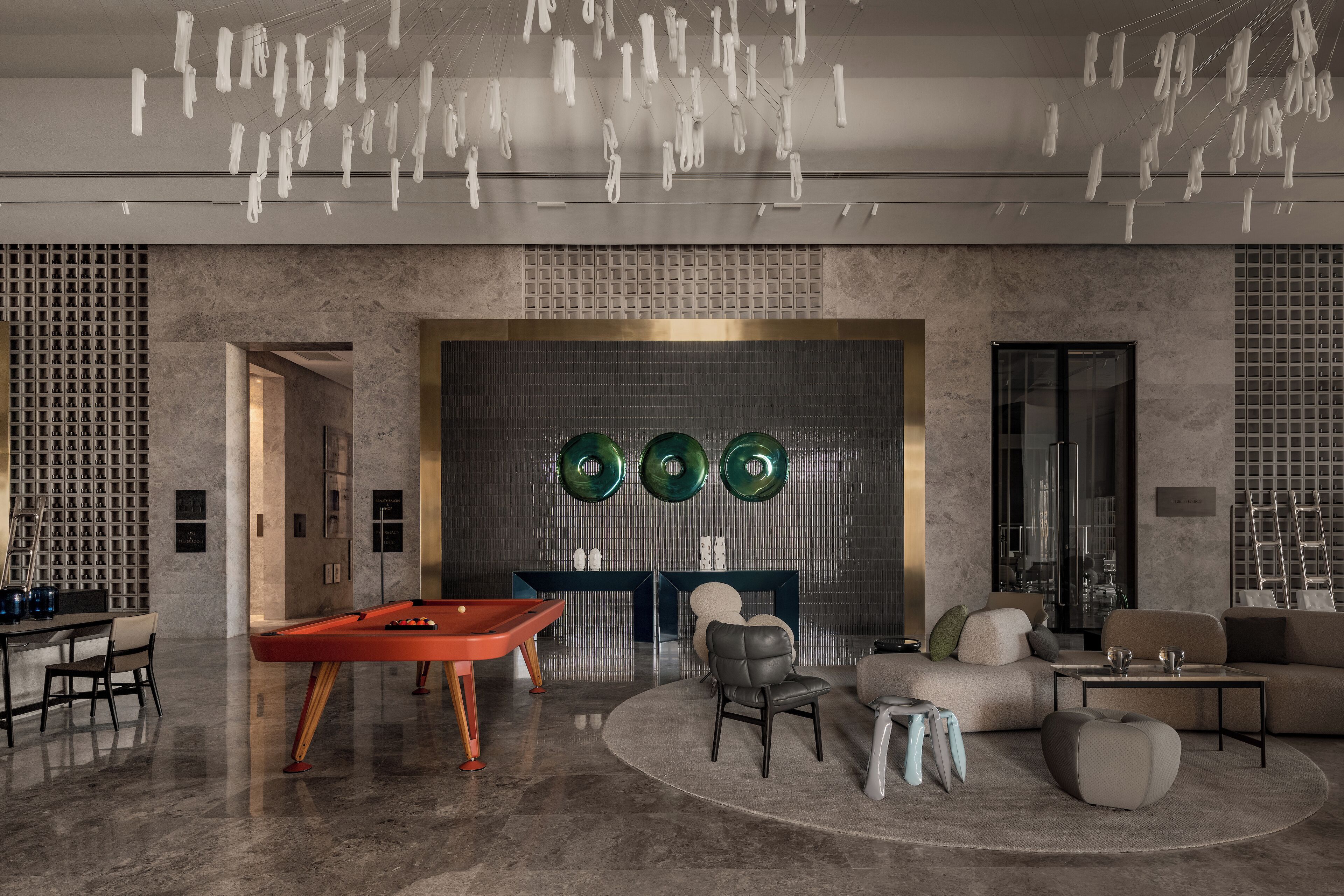 Ein modernes Wohnzimmer mit Billardtisch, bequemen Sitzgelegenheiten und einer Wand mit drei grünen, runden Spiegeln.