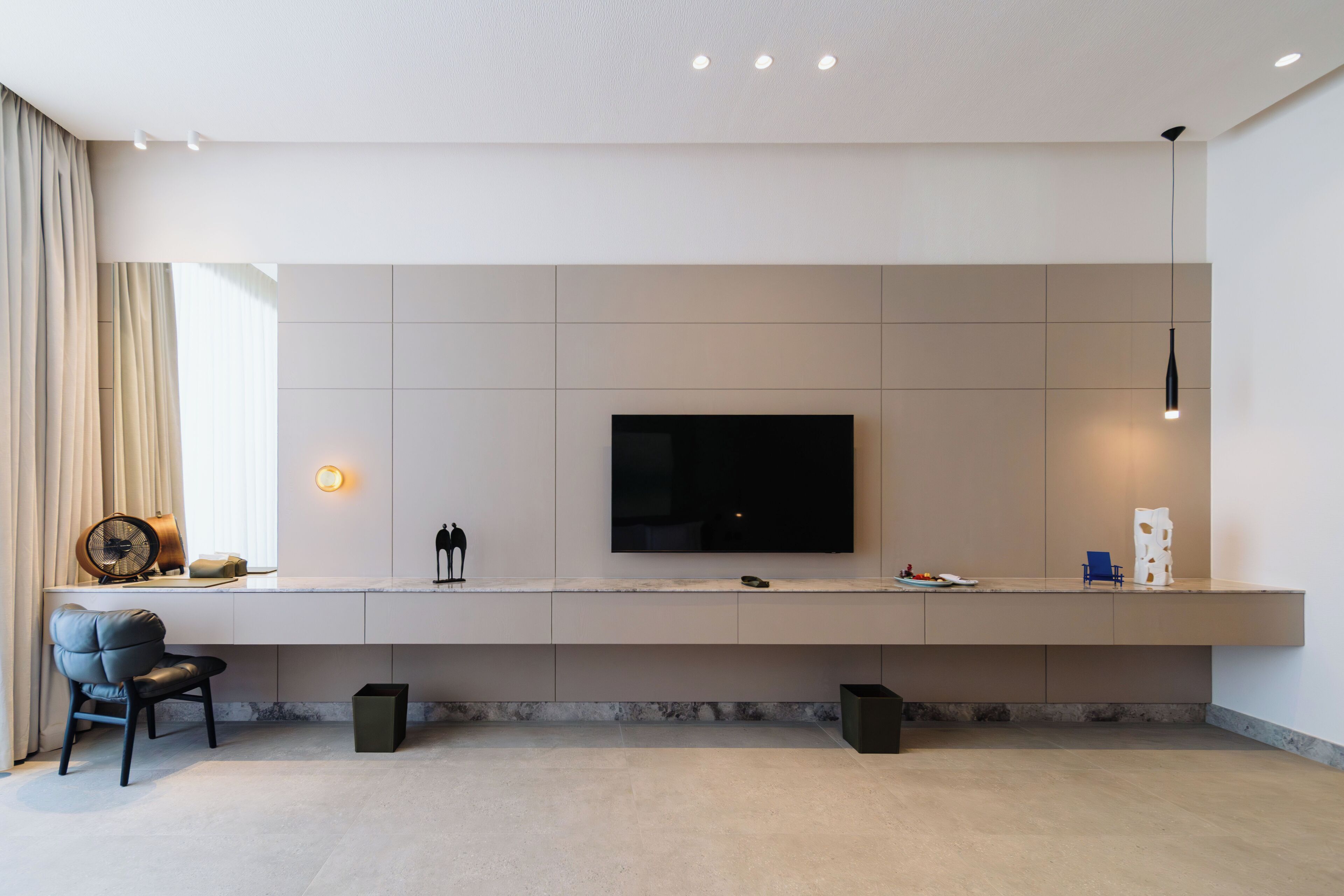 Una sala de estar moderna con un televisor de pantalla plana montado en la pared, un área de estar confortable con un sofá y una silla, y una mesita con objetos decorativos.