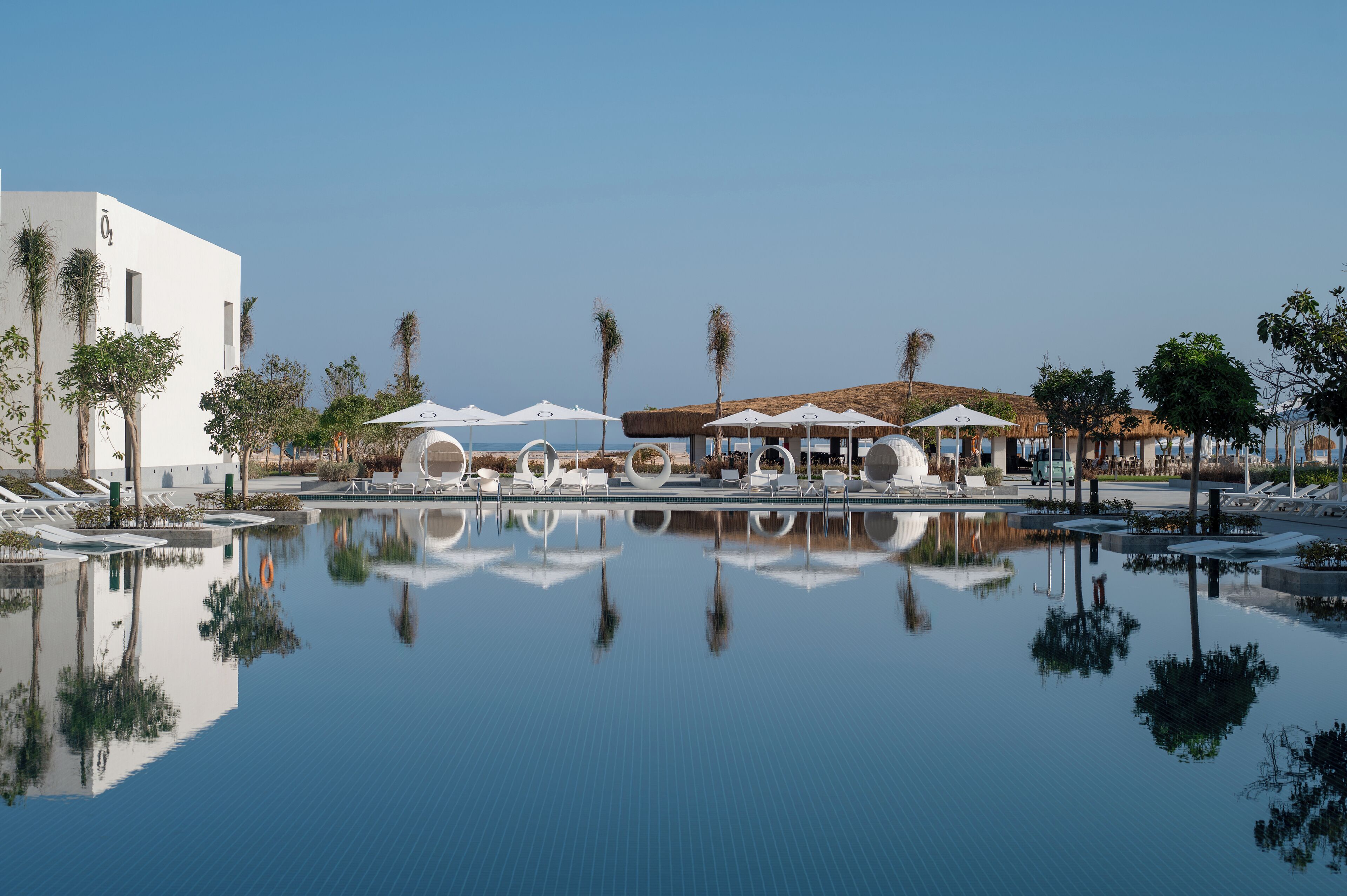 A pool area with lounge chairs and umbrellas, surrounded by palm trees and a modern building.