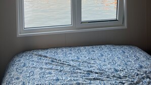 Une chambre à coucher avec un lit et une fenêtre donnant sur une marina, où l’on peut voir des bateaux et des bâtiments.