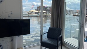 Une pièce dotée d’une grande fenêtre donnant sur un port de plaisance, d’un fauteuil noir et d’un téléviseur à écran plat.