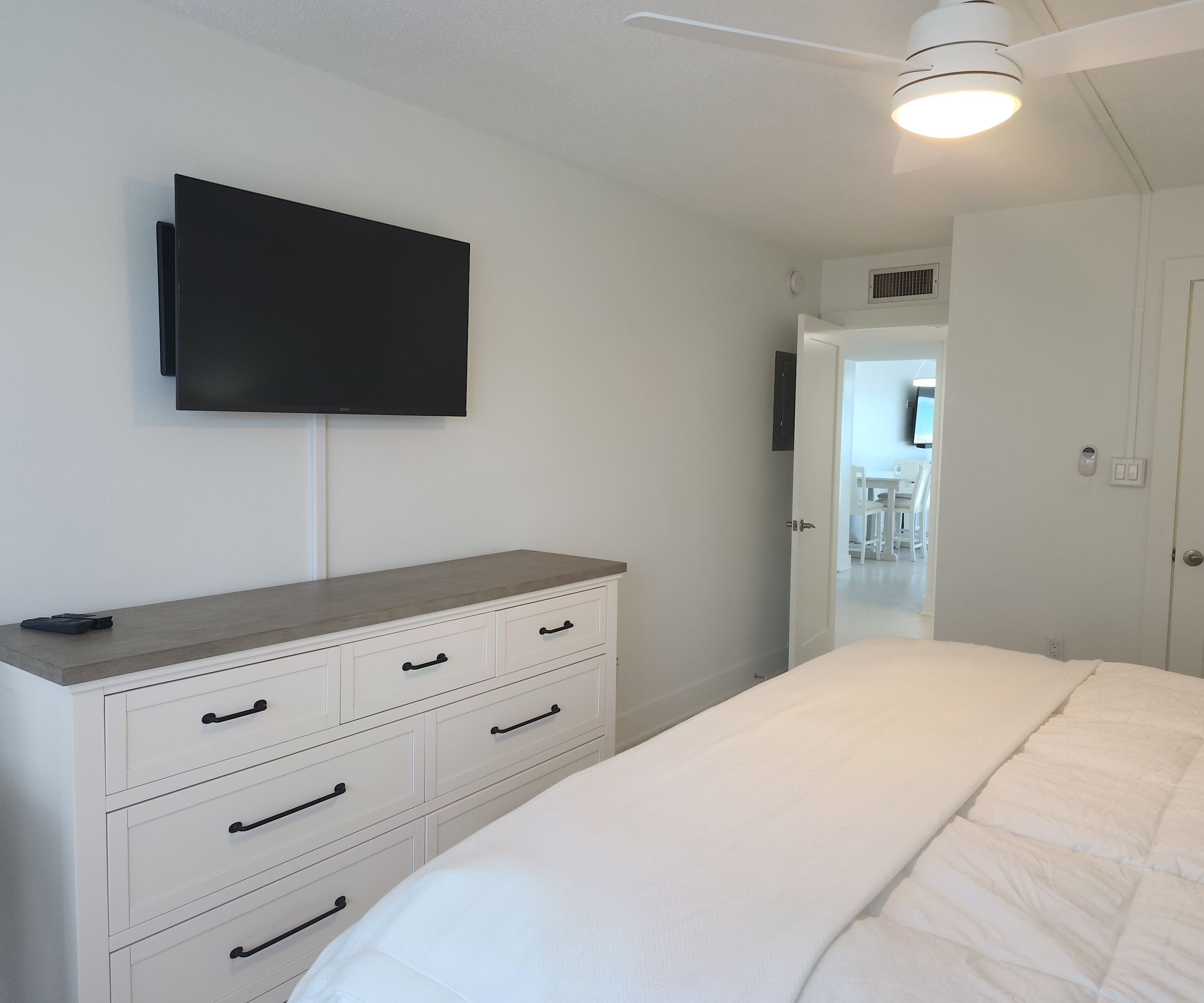 Une chambre à coucher comprenant un lit, une commode, un téléviseur fixé au mur et un ventilateur de plafond.