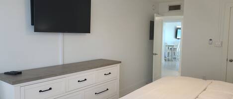 Une chambre à coucher comprenant un lit, une commode, un téléviseur fixé au mur et un ventilateur de plafond.