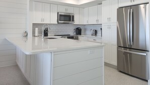 A modern kitchen with white cabinetry, a stainless steel refrigerator, a microwave, and a coffee maker.