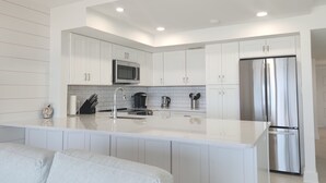 A modern kitchen with white cabinetry, a stainless steel refrigerator, and a central island with a sink.
