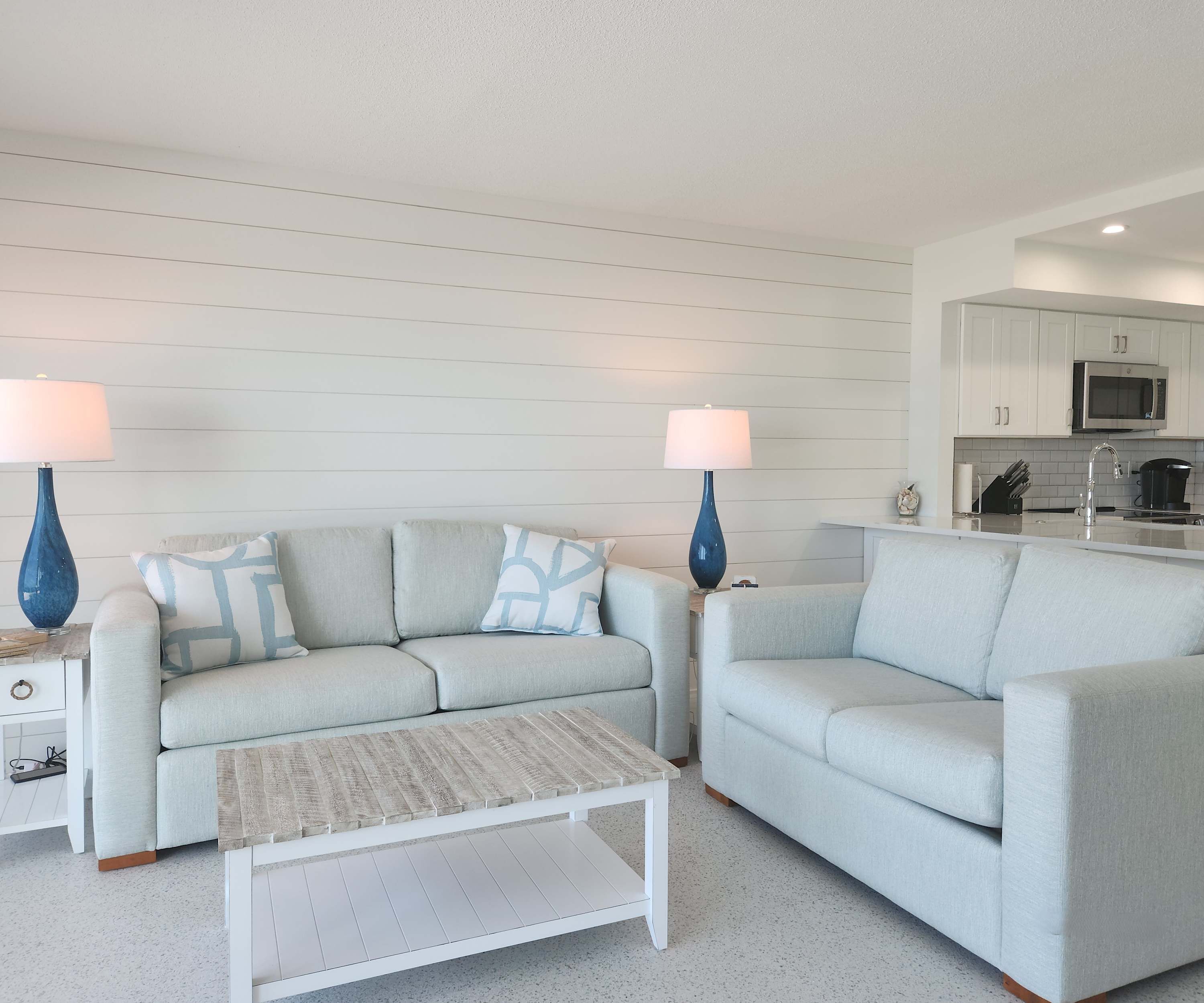 Ein Wohnzimmer mit einem hellgrauen Sofa, zwei blauen Lampen und einem Couchtisch.