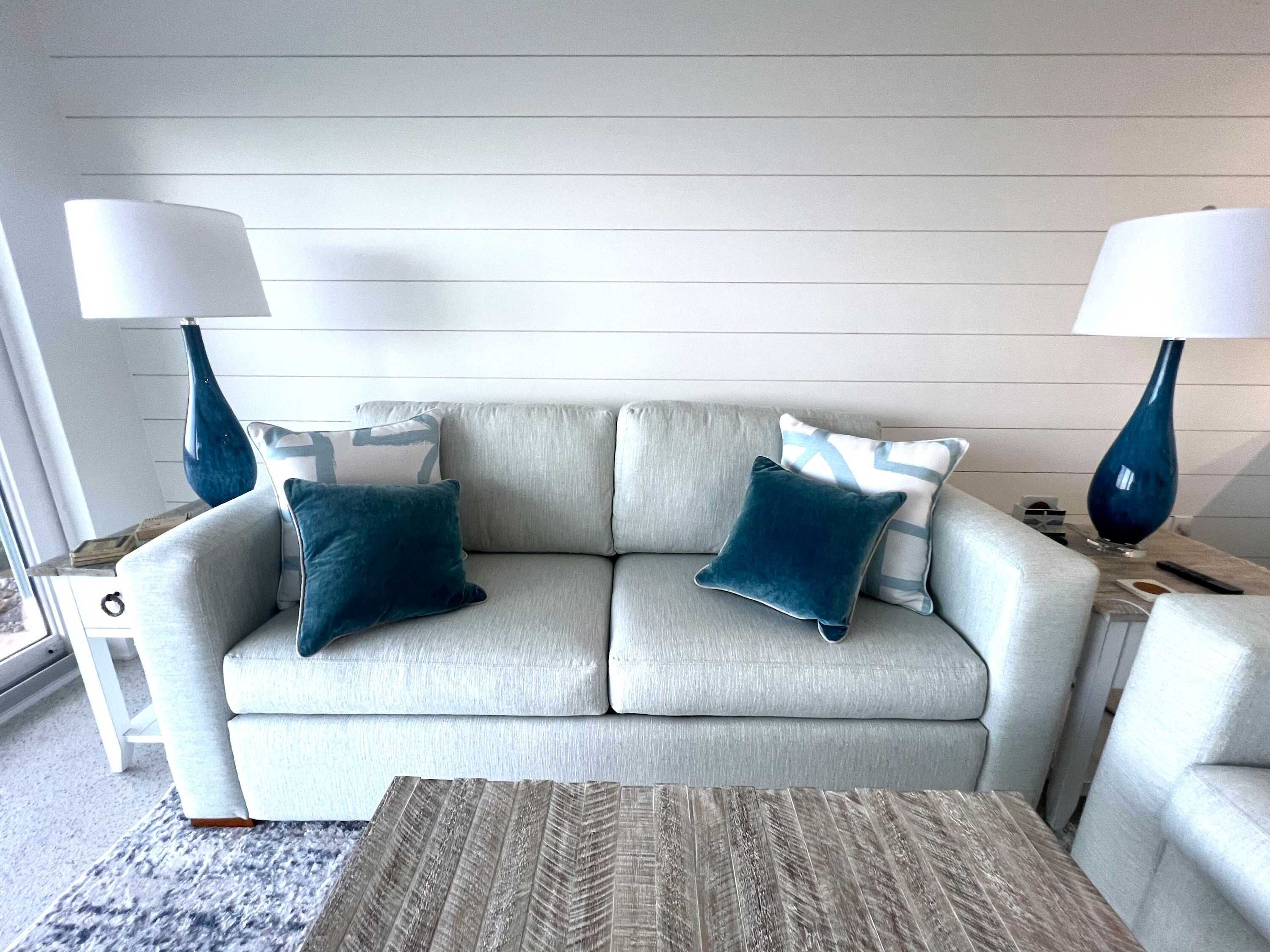 A light grey sofa with two dark blue pillows, two matching lamps, and a herringbone-patterned rug.