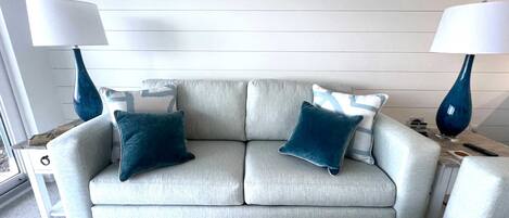 A light grey sofa with two dark blue pillows, two matching lamps, and a herringbone-patterned rug.