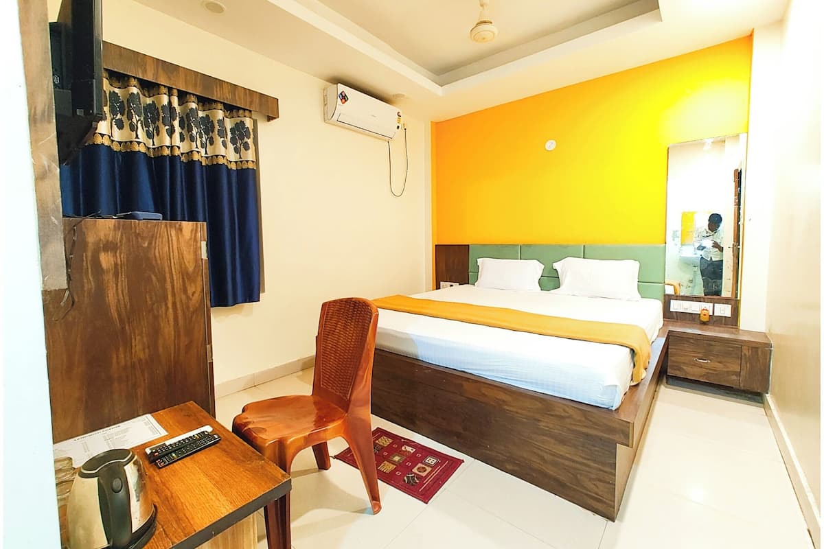 Une chambre d’hôtel comprenant un lit, un bureau avec une chaise, une petite table avec une bouilloire et un miroir.
