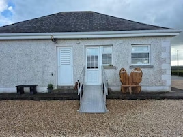 A building with a white exterior, a metal ramp leading to a door, and two wooden signs reading "Nods" and "Cottage".