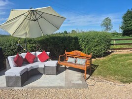 A patio with a wicker sofa, a wooden bench, and a large umbrella.