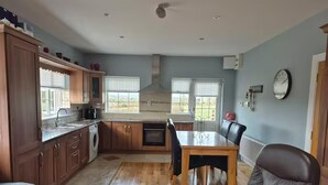 A kitchen with wooden cabinets, a dining table, and a red chair. - Tranquil Cottage Retreat in Kells, Leitrim (Mullagh)