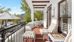 Un área de estar al aire libre con techo, mobiliario blanco, una mesa con sillas y vistas a las montañas.