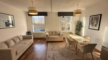 A spacious living area with a sofa, a dining table with chairs, and a large window providing a view of the city.