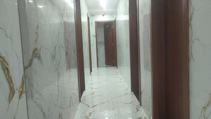 Un pasillo con suelo de mármol, puertas de madera y una lámpara en el techo.