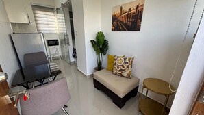 Un espace de vie compact comprenant un canapé, une petite table ronde, un coin cuisine et une porte coulissante donnant sur une autre pièce.