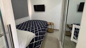 Une chambre à coucher avec un lit, une petite table ronde, un miroir et un téléviseur fixé au mur.