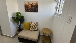 Une petite pièce bien éclairée, avec un canapé, une petite table ronde, une plante en pot et un tableau représentant un paysage urbain accroché au mur.