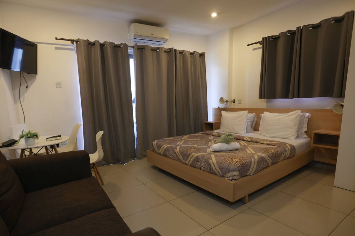 Een hotelkamer met een bed, een aan de muur bevestigde televisie, een bureau met stoel en een bank.